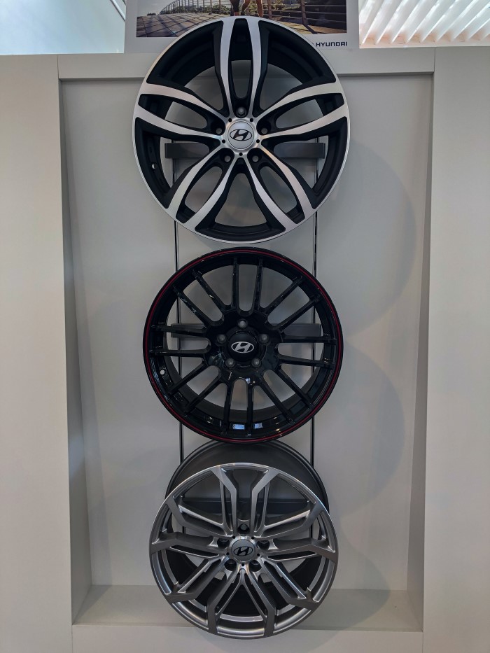 Drei moderne Leichtmetallfelgen in verschiedenen Designs, vertikal in einem Präsentationsrahmen ausgestellt.