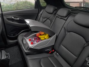 Kompakte 12-Volt-Kühlbox mit geöffnetem Deckel auf dem Rücksitz eines Fahrzeugs, gefüllt mit Getränken und Obst