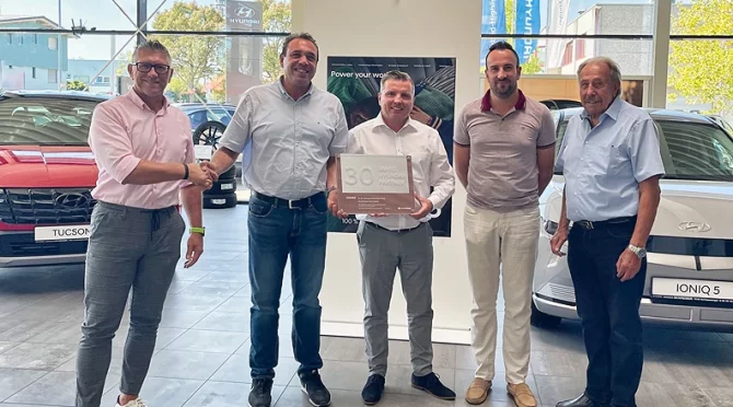Fünf Männer im Autohaus vor roten und weißen Hyundai Elektro-SUVs, helle moderne Ausstellungshalle