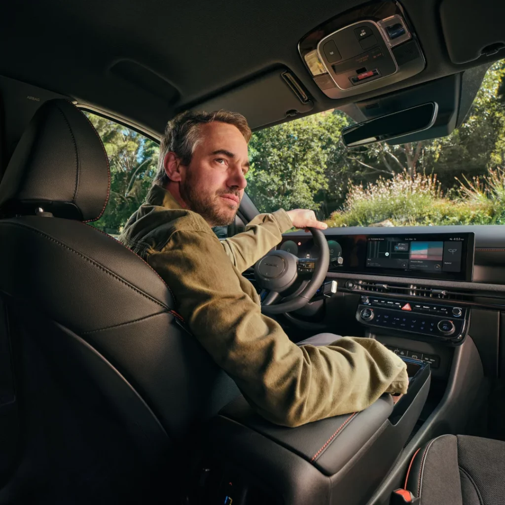 Mann im grünen Jacke fährt schwarzen Hyundai SUV, Innenraum mit roter Naht, grüne Landschaft draußen sichtbar