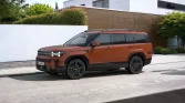 Oranger Hyundai SUV seitlich vor modernem Haus mit Holzverkleidung und grüner Hecke geparkt