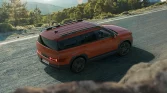 Orangener SUV in seitlicher Perspektive auf kurviger Landstraße mit grüner, hügeliger Naturkulisse