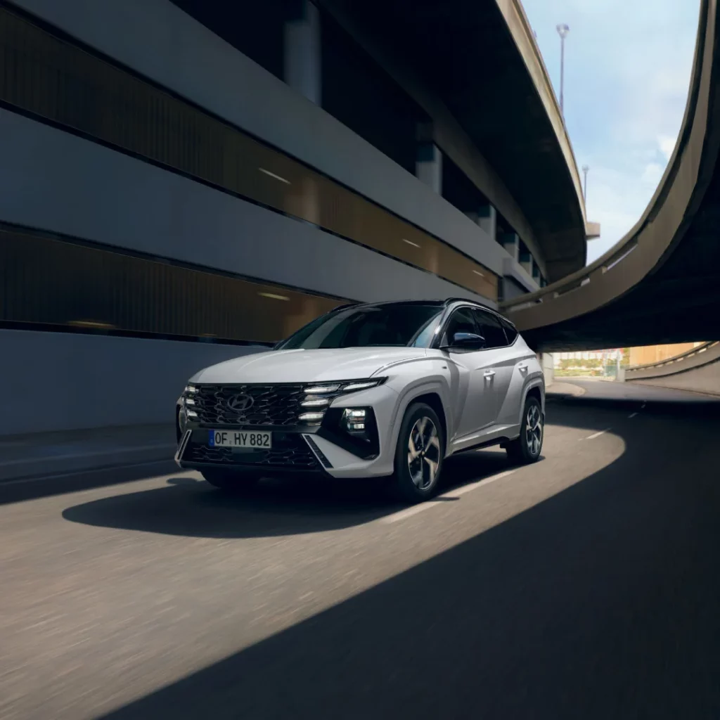 Weißer Hyundai SUV fährt dynamisch auf urbaner mehrstöckiger Straßenbrücke mit moderner Architektur