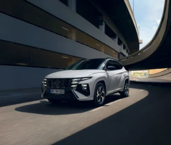 Weißer Hyundai SUV fährt dynamisch auf urbaner mehrstöckiger Straßenbrücke mit moderner Architektur