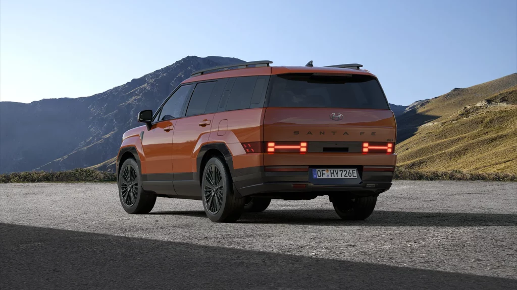Orangefarbener Hyundai SUV von hinten links, geparkt vor bergiger Landschaft bei klarem Himmel