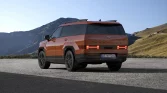 Orangefarbener Hyundai SUV von hinten links, geparkt vor bergiger Landschaft bei klarem Himmel