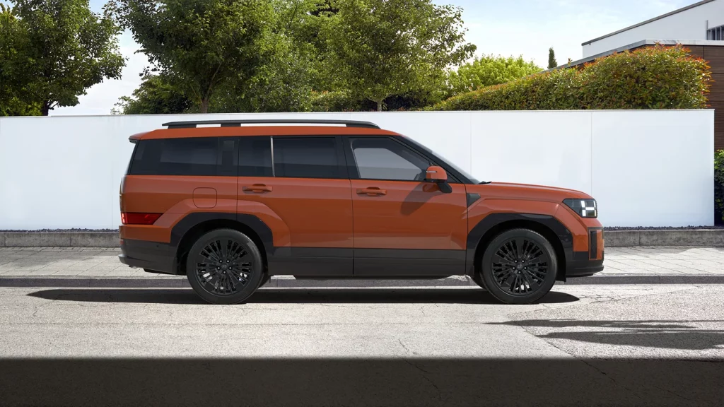 Oranger SUV seitlich vor weißer Mauer und grüner Hecke in sonniger Wohngegend geparkt