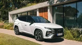 Weißer moderner SUV auf Zufahrt vor zeitgenössischem Haus mit grüner, bewachsener Umgebung