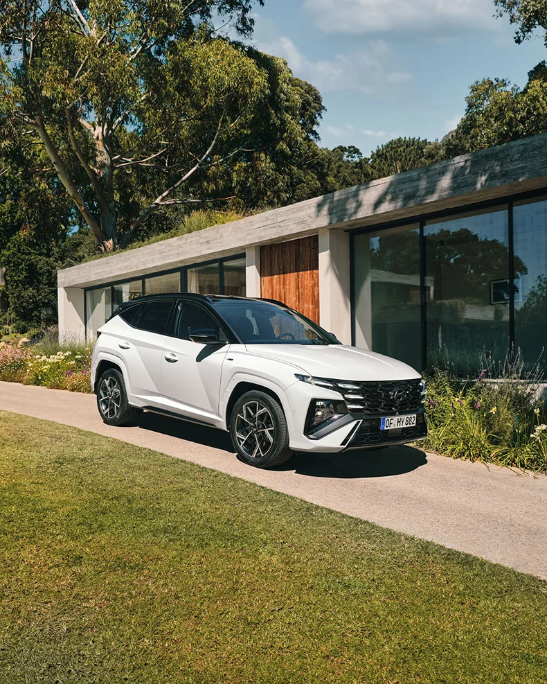 Weißer moderner SUV auf Zufahrt vor zeitgenössischem Haus mit grüner, bewachsener Umgebung
