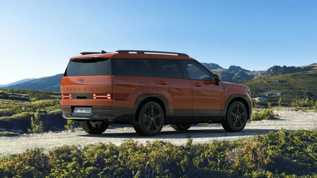Oranger Hyundai SUV von hinten auf Offroad-Pfad in hügeliger Naturlandschaft bei klarem Himmel