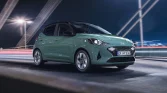 Grüner Hyundai Kleinwagen in 3/4-Frontansicht fahrend auf beleuchteter Stadtbrücke bei Nacht