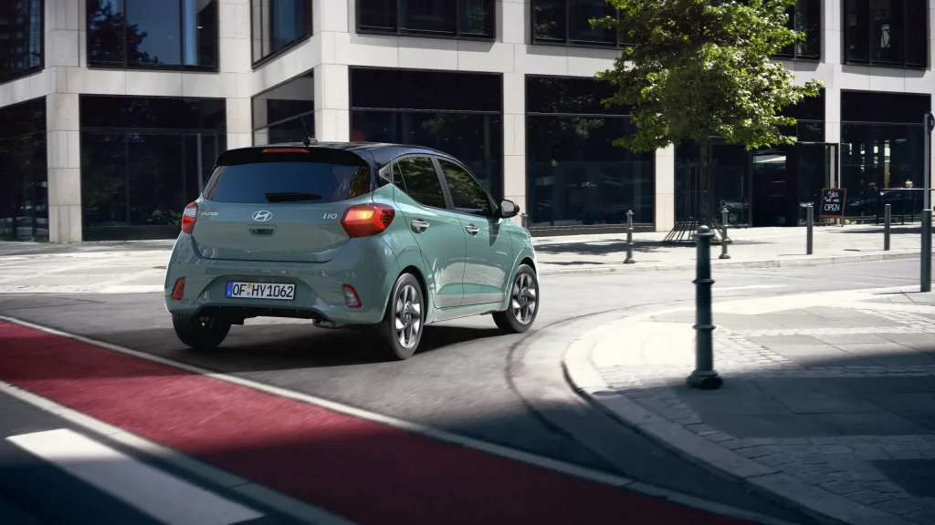 Hellgrüner Hyundai Kleinwagen von hinten beim Abbiegen in moderner, urbaner Straße mit Café und Architektur