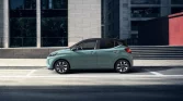 Pastellgrüner moderner Kleinwagen seitlich geparkt vor hellem urbanem Gebäude mit Glasbarrieren und roten Wänden