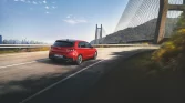 Roter Hyundai Kompaktwagen von hinten fahrend auf Brücke mit Bergen und Stadt im Hintergrund