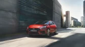 Roter Hyundai Kompaktwagen in Bewegung auf breiter Straße vor moderner Stadtlandschaft bei Tageslicht