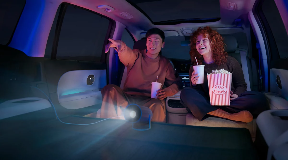 Zwei Personen im modernen, geräumigen Elektro-SUV bei Nacht genießen Filmabend mit Projektor und Snacks im Innenraum.