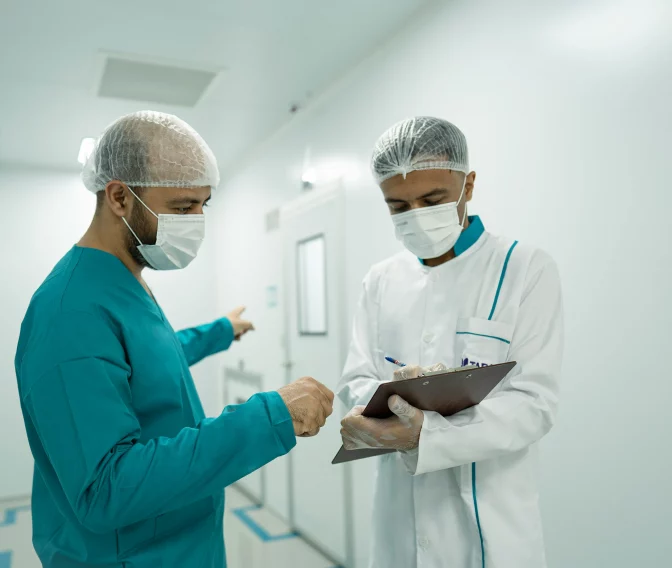 Zwei medizinische Fachkräfte mit OP-Masken sprechen in hellem Krankenhausflur über Patientendaten