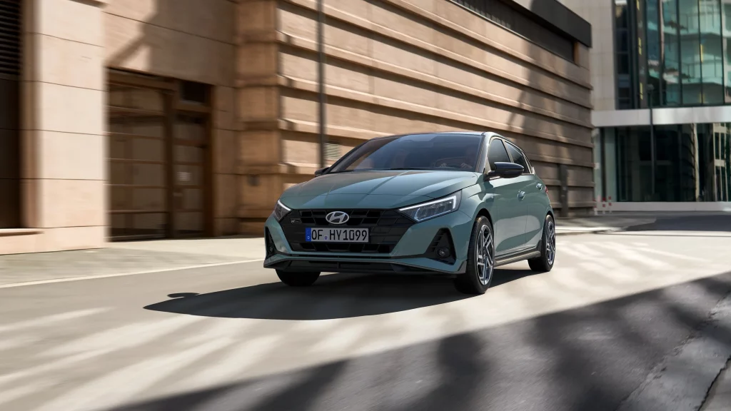 Tealfarbener Hyundai Kleinwagen in Fahrperspektive vor modernen urbanen Gebäuden bei Tageslicht