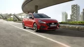 Roter Hyundai Kombi in sportlichem Design, frontal vor moderner Stadtarchitektur bei Tageslicht fahrend