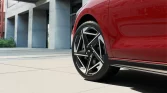 Roter Hyundai Kompaktwagen Seitenansicht mit sportlichem Rad vor modernem urbanem Hintergrund