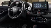 Innenraum eines sportlichen Hyundai Kompaktwagens mit rotem Akzent im Cockpit, urbaner Hintergrund sichtbar.