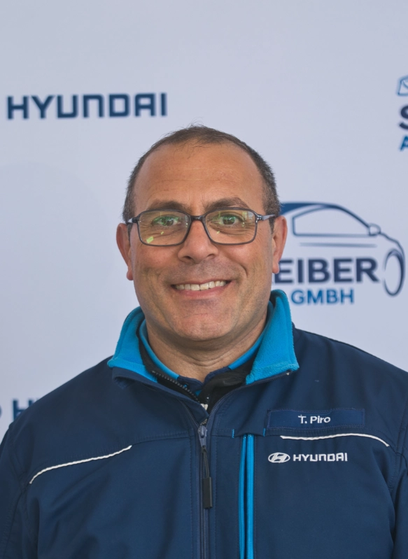 Mann mit Brille in Hyundai-Jacke vor Firmenwand, freundliches Lächeln, professionelle Eventatmosphäre