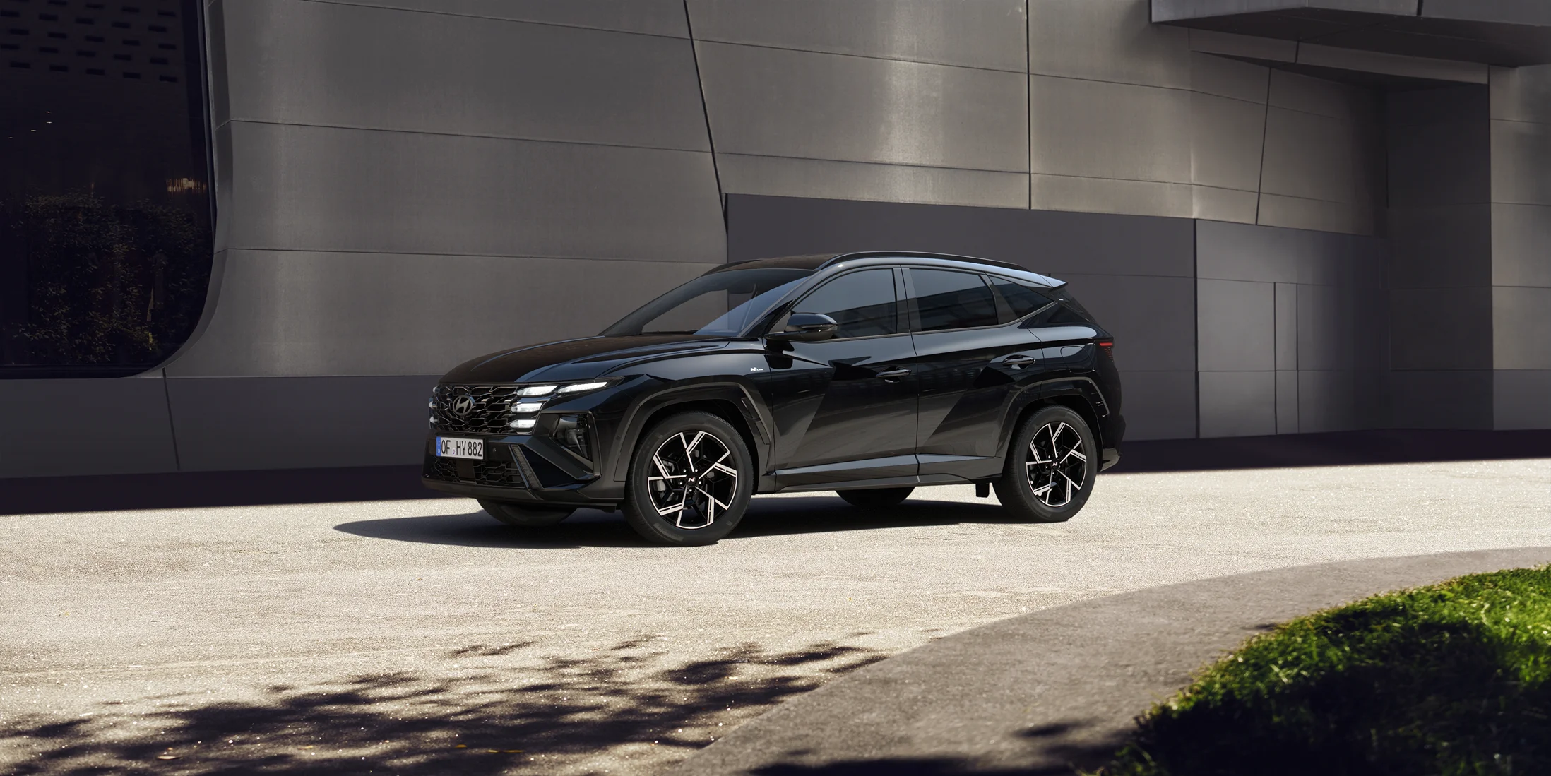 Black month 4 Schwarzer moderner SUV seitlich vor urbanem Industriegebäude und Grünfläche bei Tageslicht geparkt