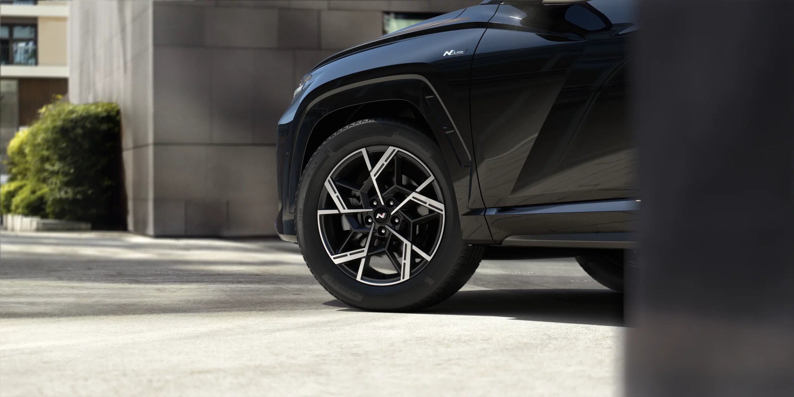 Black month 9 Schwarzer Hyundai SUV in Nahaufnahme, Fokus auf Rad, vor modernem Gebäude und Grünpflanzen geparkt