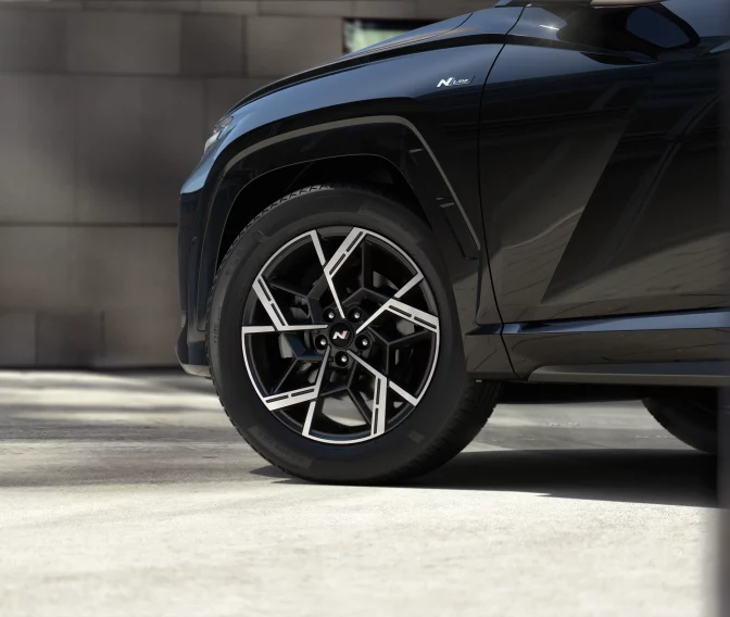 Schwarzer Hyundai Kompaktwagen, Nahaufnahme Rad und N Line Emblem, urbaner Hintergrund mit Pflanzen und Gebäude