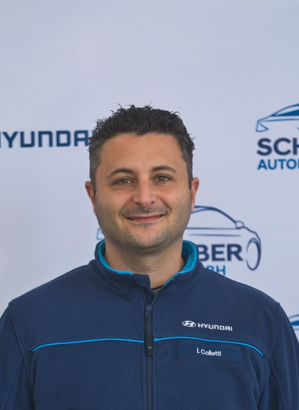 Mann in Hyundai-Uniform vor blau-weißem Auto-Branding, freundlich lächelnd, professionelles Porträt