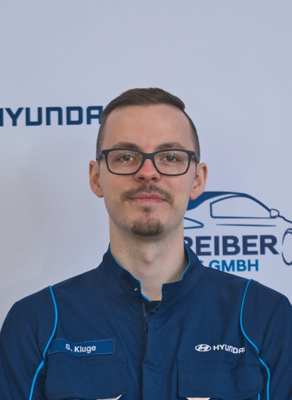 Mann in Hyundai-Uniform vor Firmenlogo von Reiber GmbH, freundlich und professionell posierend