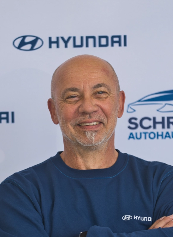 Mann mit grauem Bart in blauem Hyundai-Sweatshirt vor Hyundai-Logo auf Firmenveranstaltung