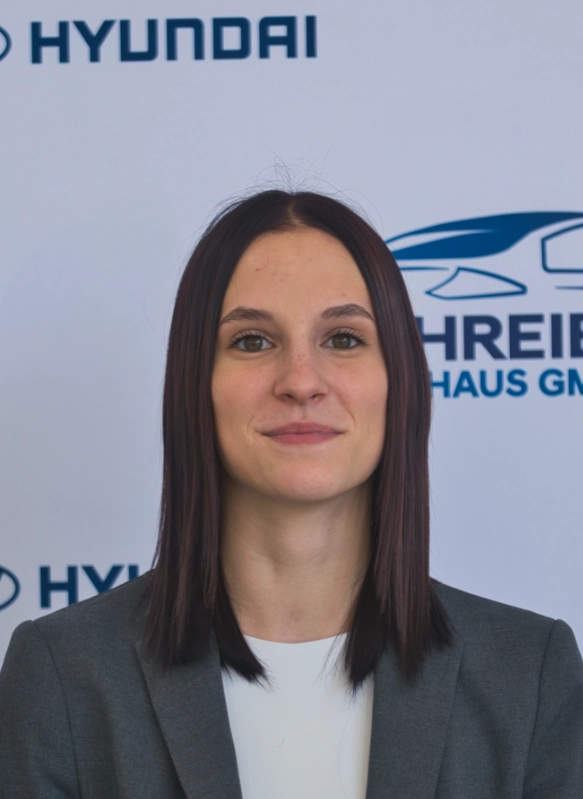 Junge Frau in grauem Blazer vor Hyundai-Logo stehend, professionelles Porträt, freundlich und kompetent