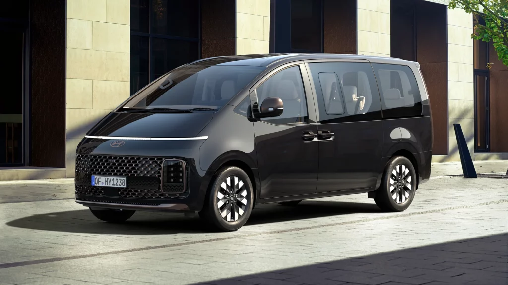 Schwarzer moderner Minivan in 3/4-Frontansicht vor zeitgenössischem Gebäude und urbaner Umgebung geparkt