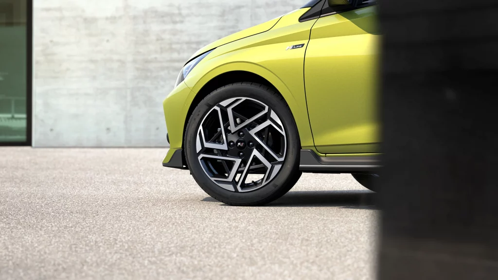 Gelb-grüner Hyundai Kompaktwagen vorn links mit sportlicher Felge vor heller Wand geparkt