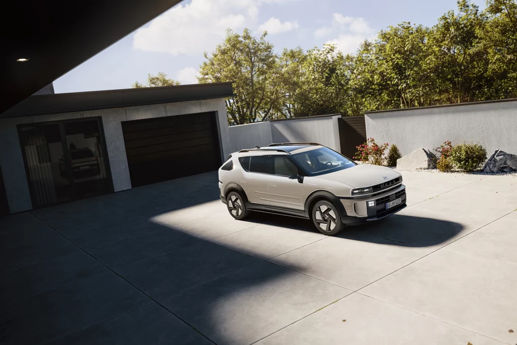 Cremefarbener kompakter Crossover in Dreiviertelansicht, vor modernem Haus auf Einfahrt geparkt