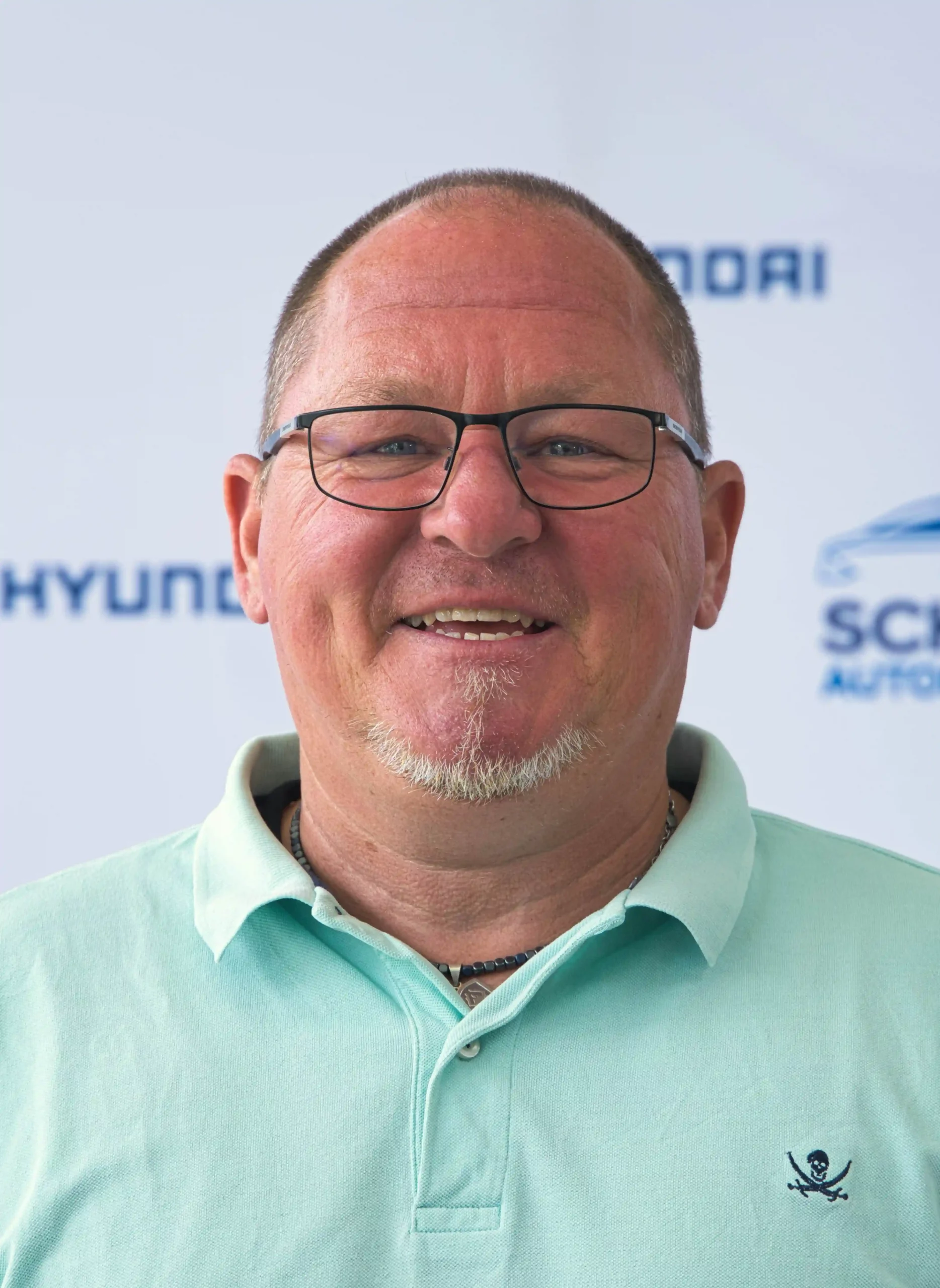 Porträt von Andreas Bär, lächelnder Mann mit Brille vor Autohaus Schreiber-Hintergrund