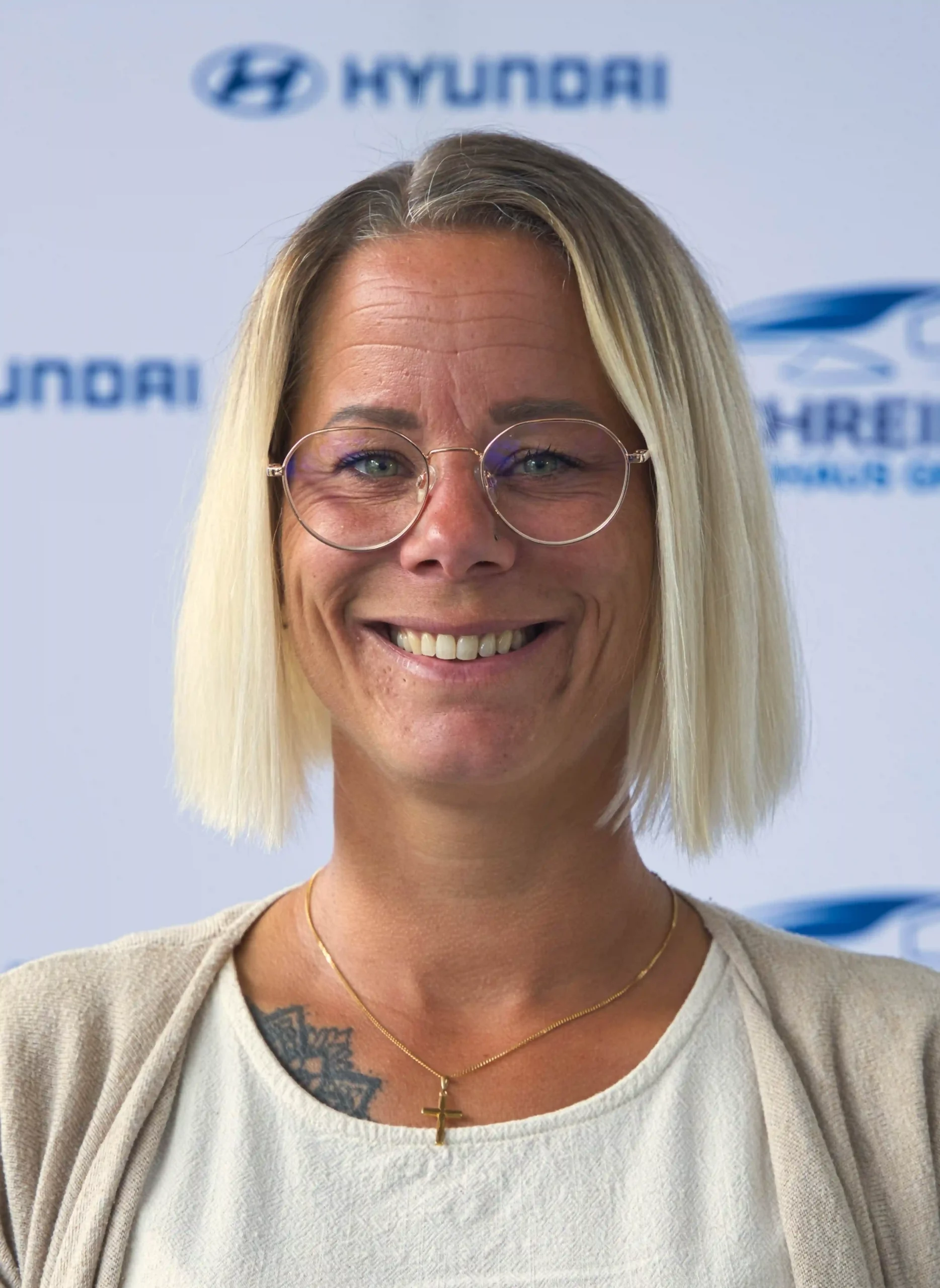 Porträt einer lächelnden blonden Frau mit Brille vor Autohaus Schreiber-Logo