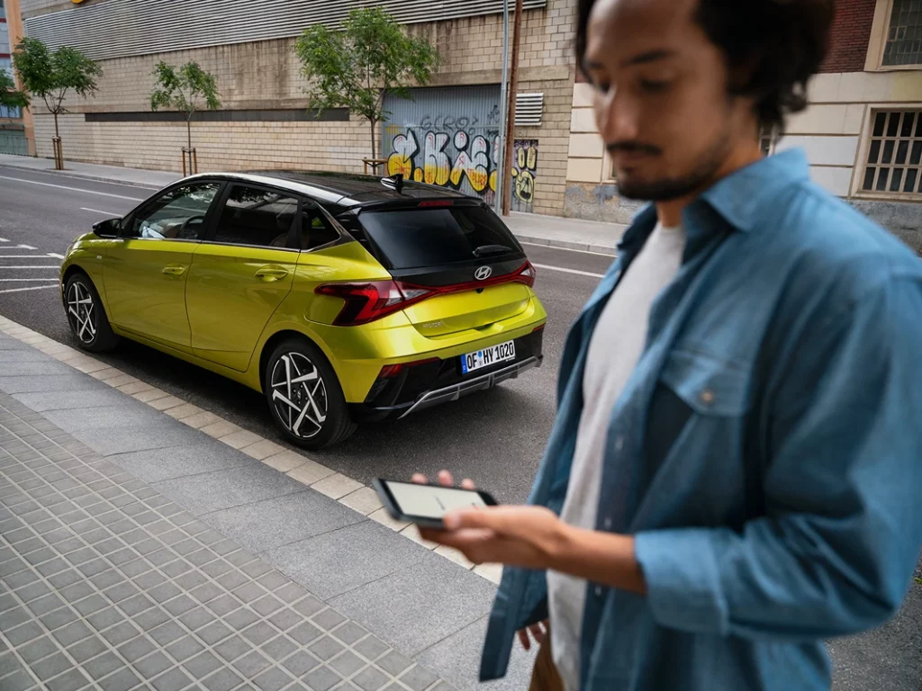 Leuchtend limettengrüner Hyundai Kompaktwagen Heck-Dreiviertelansicht an städtischem Gehweg, unscharfer Mann.