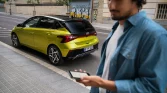 Leuchtend limettengrüner Hyundai Kompaktwagen Heck-Dreiviertelansicht an städtischem Gehweg, unscharfer Mann.