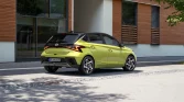Limettengrüner Hyundai Kompaktwagen, Heck-Dreiviertelansicht, geparkt vor modernem Gebäude