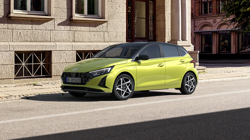 Gelbgrüner Hyundai Kompaktwagen, Drei‑Viertel‑Frontansicht, geparkt vor städtischer Steinfassade