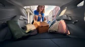 Blick aus offenem Kofferraum eines grauen Hyundai Kompaktwagens, Frau lädt Picknickkorb auf städtischer Straße