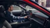 Innenraum eines roten Hyundai‑Kompaktwagens, Fahrer bedient Infotainment, urban geparkt.