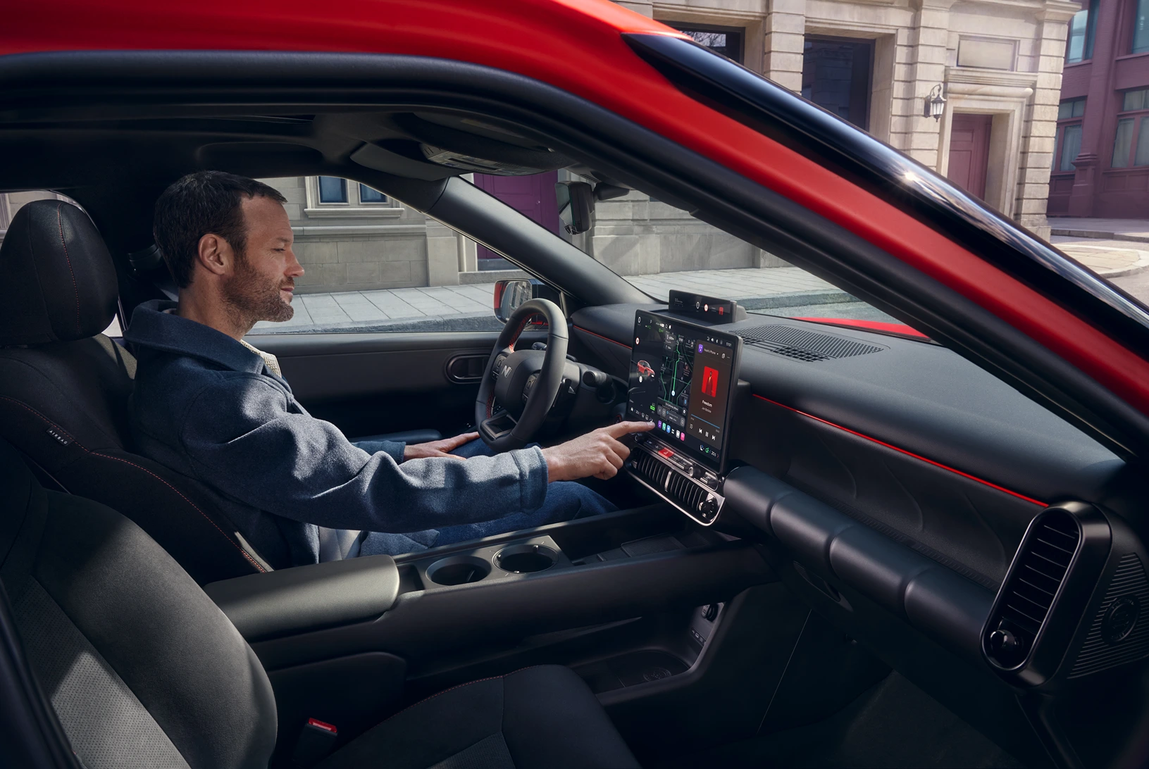 Innenraum eines roten Hyundai‑Kompaktwagens, Fahrer bedient Infotainment, urban geparkt.