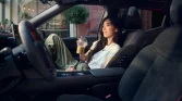 Hyundai Kompaktwagen, dunkler Innenraum seitliche Aufnahme, Frau mit Eiskaffee, geparkt vor Café