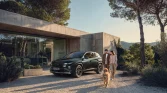 Dunkelgrüner Hyundai-SUV seitlich geparkt vor modernem Haus, zwei Personen mit Hund.