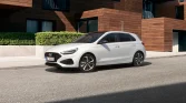 Weißer Hyundai Kompaktwagen, Dreiviertel-Frontansicht links vor modernem Wohngebäude geparkt