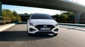 Weißer Hyundai Kompakt-Crossover frontal in Fahrt auf Straße unter Brücke vor grünen Bäumen