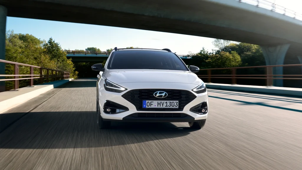 Weißer Hyundai Kombi frontal fahrend auf Brücke, Straße und Bäume im Hintergrund